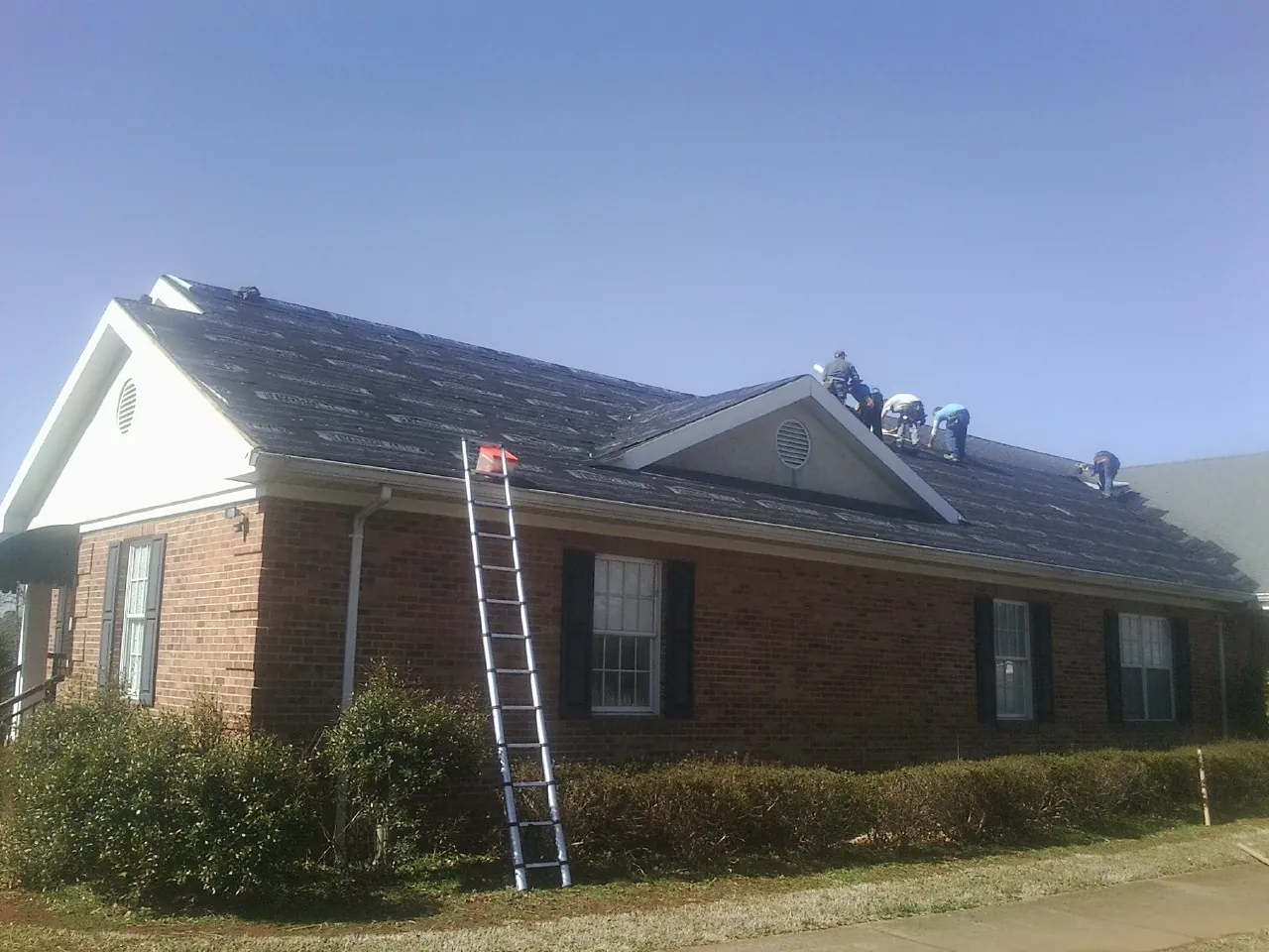 Crew tearing shingles off a brick ranch roof with a ladder set — Metal Roof Repair work by our crew in Kingston