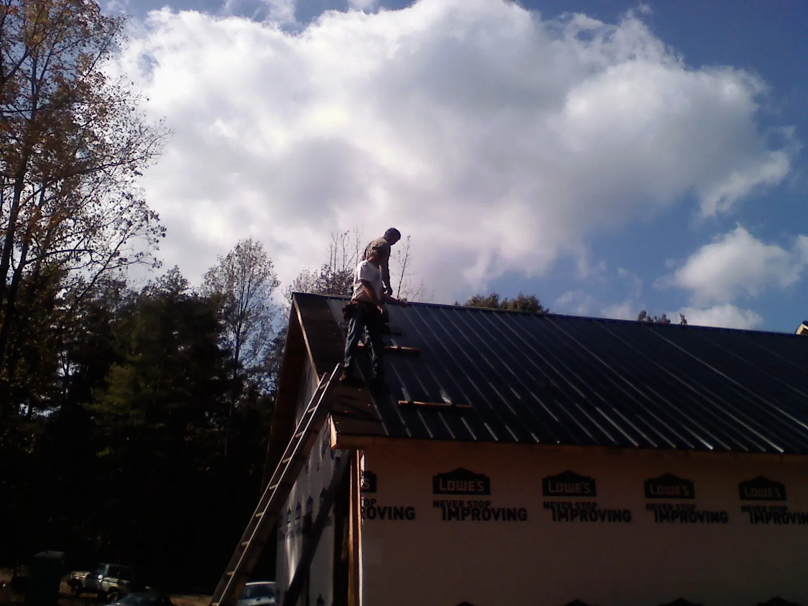 Roofer fastening dark metal panels high against a cloudy sky, from a Roof Inspection job in Kingston