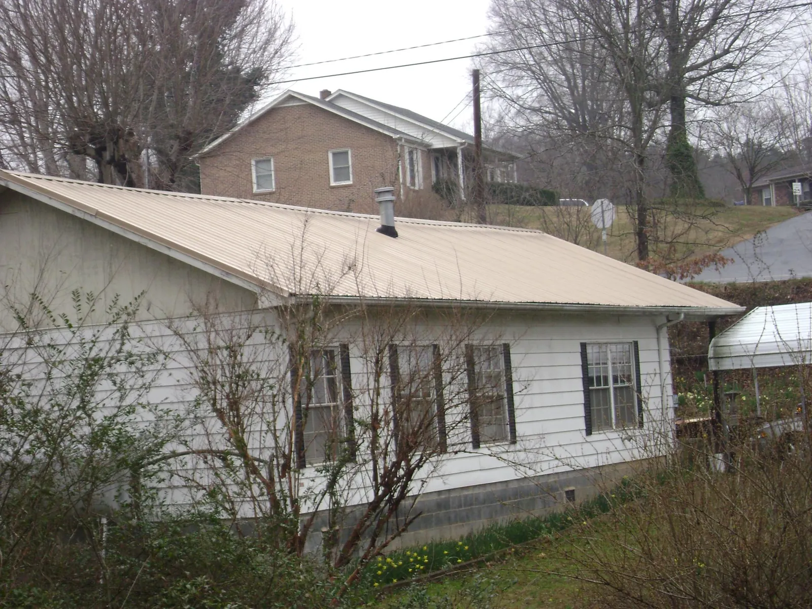 Tan metal roof on a white sided house set into a hillside — Commercial Roofing by Roofing Brothers in Kingston